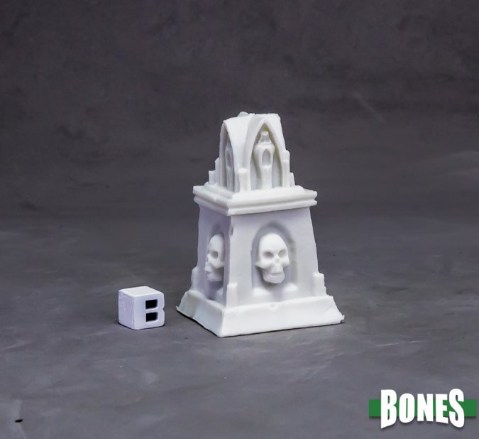 White miniature tombstone with skull designs on a gray background, featuring the 'BONES' brand. Reaper Miniatures graveyard altar. Unpainted