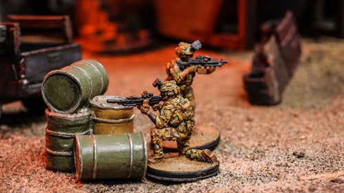 2 Green Beret Miniatures surveying their surroundings. 1 miniature kneels behind a oil drum. The other miniature looks out in its surroundings.