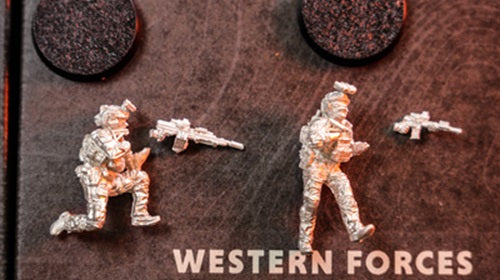2 unpainted green beret force miniatures beside their weapons.