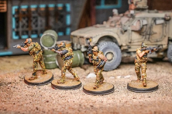 4 Green beret force miniatures in different poses in a apocalyptic setting with a armored vehicle and dilapidated house behind them.